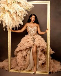 a woman in a dress is holding a frame with feathers on it and posing for the camera