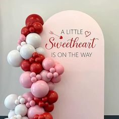 a balloon arch is decorated with red, white and pink balloons that read a little sweetheart is on the way