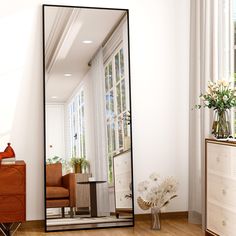 a large mirror sitting on top of a wooden floor next to a vase with flowers