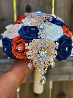 a bridal bouquet with blue, orange and white flowers is held by someone's hand