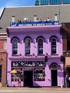 a purple building with people standing on top of it in front of the sign welcome to music city