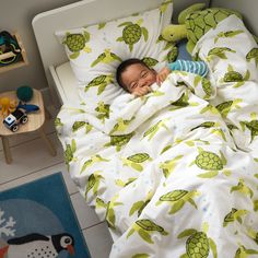 a small child is laying in bed with a stuffed turtle on the floor next to him