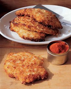 three fried chicken patties on a white plate next to a small bowl of seasoning