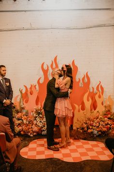 two people are hugging each other in front of a wall with fire and flowers on it