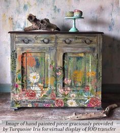 an old dresser with flowers painted on it and a cake sitting on top of it