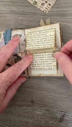 two hands are holding an old book open on a wooden table with other items around it