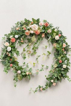 an arrangement of flowers and greenery arranged on a white wall in the shape of a circle