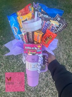 a person holding a cup filled with candy and other snacks on top of the grass