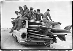 a group of people sitting on top of a car filled with surfboards