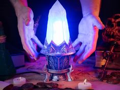 two hands holding a lit candle on top of a table with other items around it