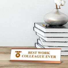 a stack of books sitting next to a silver vase on top of a wooden table