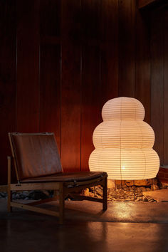 a lamp sitting on top of a wooden floor next to a chair and ottoman in front of a wall