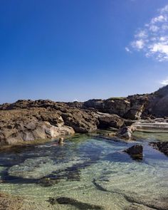 the water is crystal clear and there are some rocks in the foreground with blue skies above