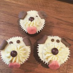 three cupcakes with frosting and dog faces on them sitting on a table