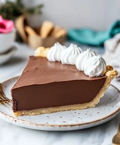 a piece of chocolate pie with whipped cream on top sitting on a plate next to a fork