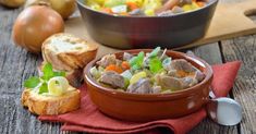 a bowl filled with meat and vegetables on top of a red cloth next to bread