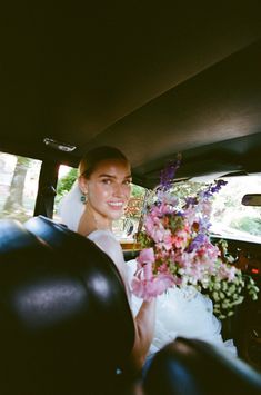 a bride in the back seat of a car holding a bouquet of flowers on her wedding day