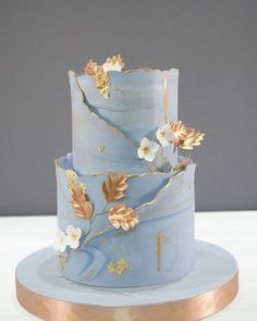 a three tiered blue cake with gold leaves and flowers