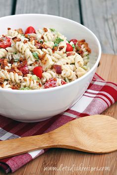 a white bowl filled with pasta salad on top of a wooden table next to a spoon