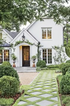 a white house with stone walkway leading to the front door and entry way, surrounded by greenery