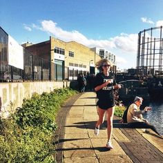 a woman running down a path next to the water with buildings in the back ground