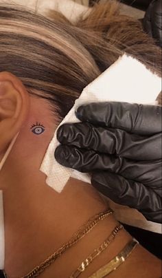 a woman with a small eye tattoo on her left side behind the ear is a pair of black gloves