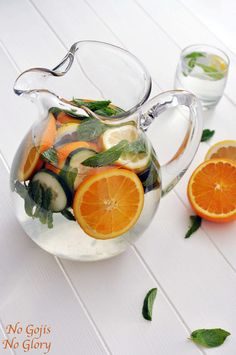 a pitcher filled with sliced oranges, cucumbers and mint on top of a white table