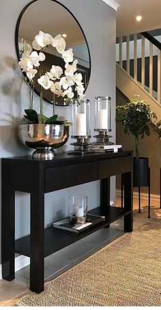 a black console table with flowers and candles on it in front of a stair case