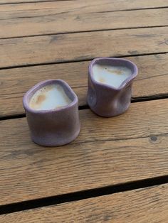 two small cups sitting on top of a wooden table next to each other, one filled with liquid