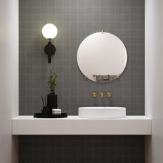 a white sink sitting under a round mirror on top of a bathroom counter next to a black and white tiled wall