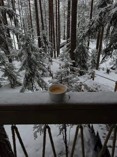 a cup of coffee sitting on top of a window sill in the middle of a snow covered forest