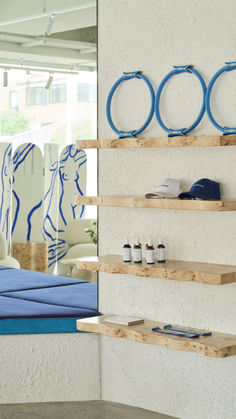 three wooden shelves holding various items in front of a wall with blue artwork on it