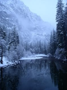 snow covered trees surrounding a lake in the middle of a snowy mountain range, with water running through it