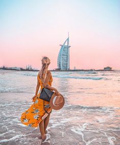 a woman walking on the beach in front of burj al arab hotel at sunset