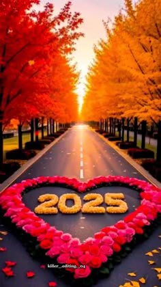 a heart shaped sign on the side of a road surrounded by flowers and trees in fall colors