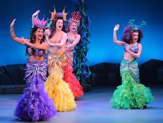 three women in colorful dresses are dancing on stage