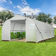 a greenhouse with the door open and plants growing inside it on grass in front of a house