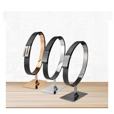 three metal rings are on display in front of a white wall and wooden table top