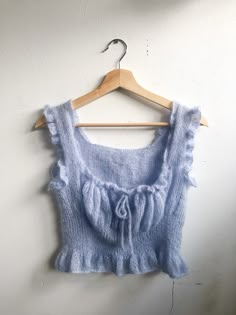 a blue top hanging on a wooden hanger with a white wall in the background