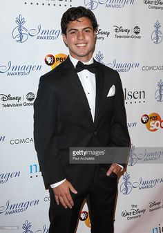 a man in a tuxedo poses on the red carpet at an awards event