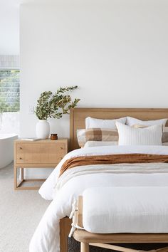 a bed with white sheets and pillows in a bedroom next to a plant on the nightstand