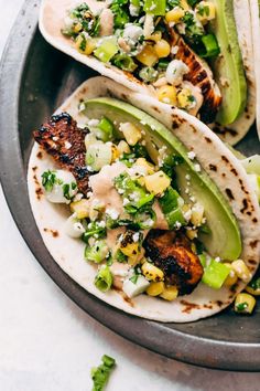 three tacos on a plate with avocado, corn and other toppings