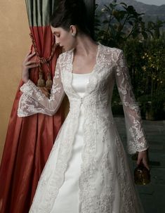 a woman in a white wedding dress standing next to a red curtain and holding a purse