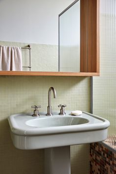 a white sink sitting under a bathroom mirror next to a wooden shelf with towels on it