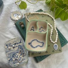 an assortment of jewelry sits on a table next to a book and flower pot with green leaves in the background