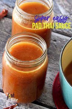 two jars filled with sauce sitting on top of a wooden table