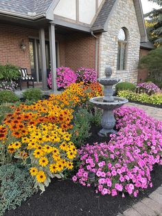 colorful flowers in front of a house with a birdbath and water fountain on the side