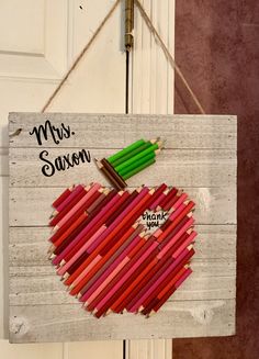 a wooden sign with colored pencils in the shape of an apple hanging on a door