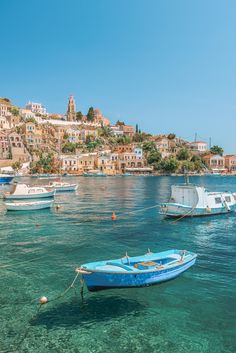 several small boats floating in the water next to a city on top of a hill