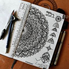 an open notebook with black and white doodles on the pages next to some pens